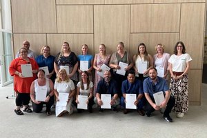 Gruppenfoto von 16 Absolventinnen und Absolventen nach dem erfolgreichen Abschluss einer Weiterbildung. Die Gruppe steht gemeinsam in den Räumlichkeiten der Zentralschule der Alexianer, dem Bildungszentrum für Gesundheit und Soziales. Die Teilnehmenden lächeln in die Kamera und halten gemeinsam den Abschluss ihrer Weiterbildung fest.